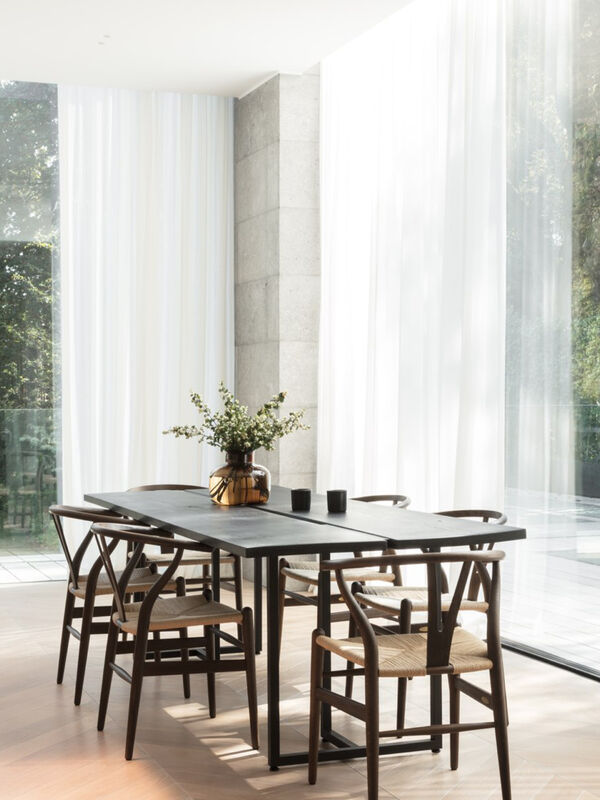 Dining area with wishbone chairs and dark wood table by floor-to-ceiling curtained windows