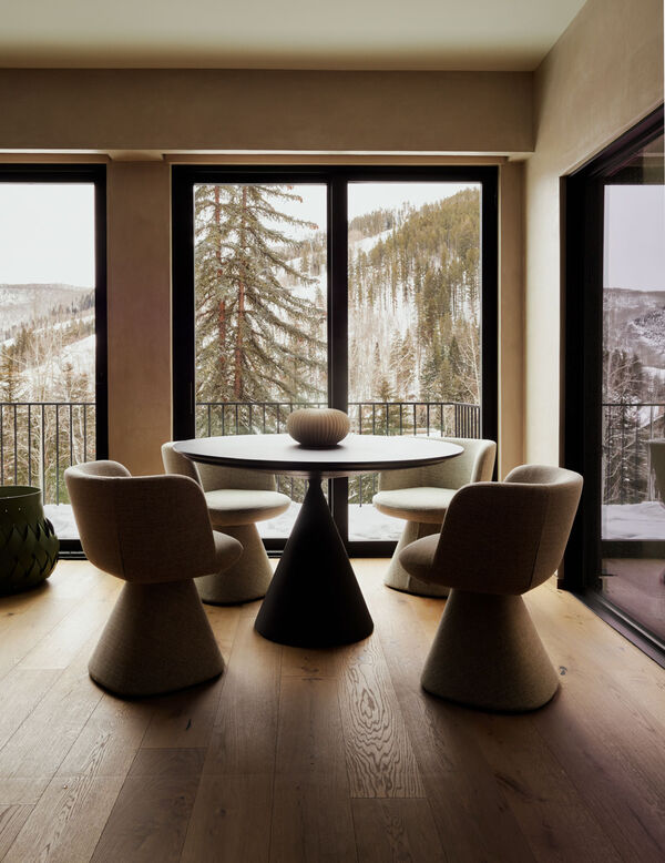 Minimalist dining room with round table, upholstered chairs, and forest view through large windows
