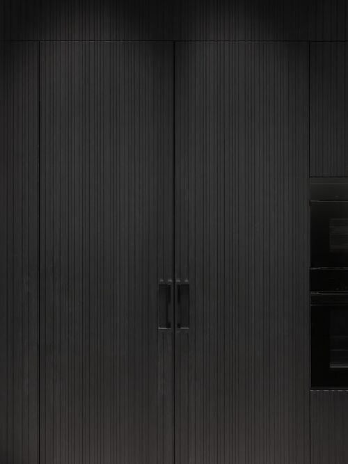 Close-up of a matte black fluted cabinet front with an inset handle, shown alongside built-in black appliances