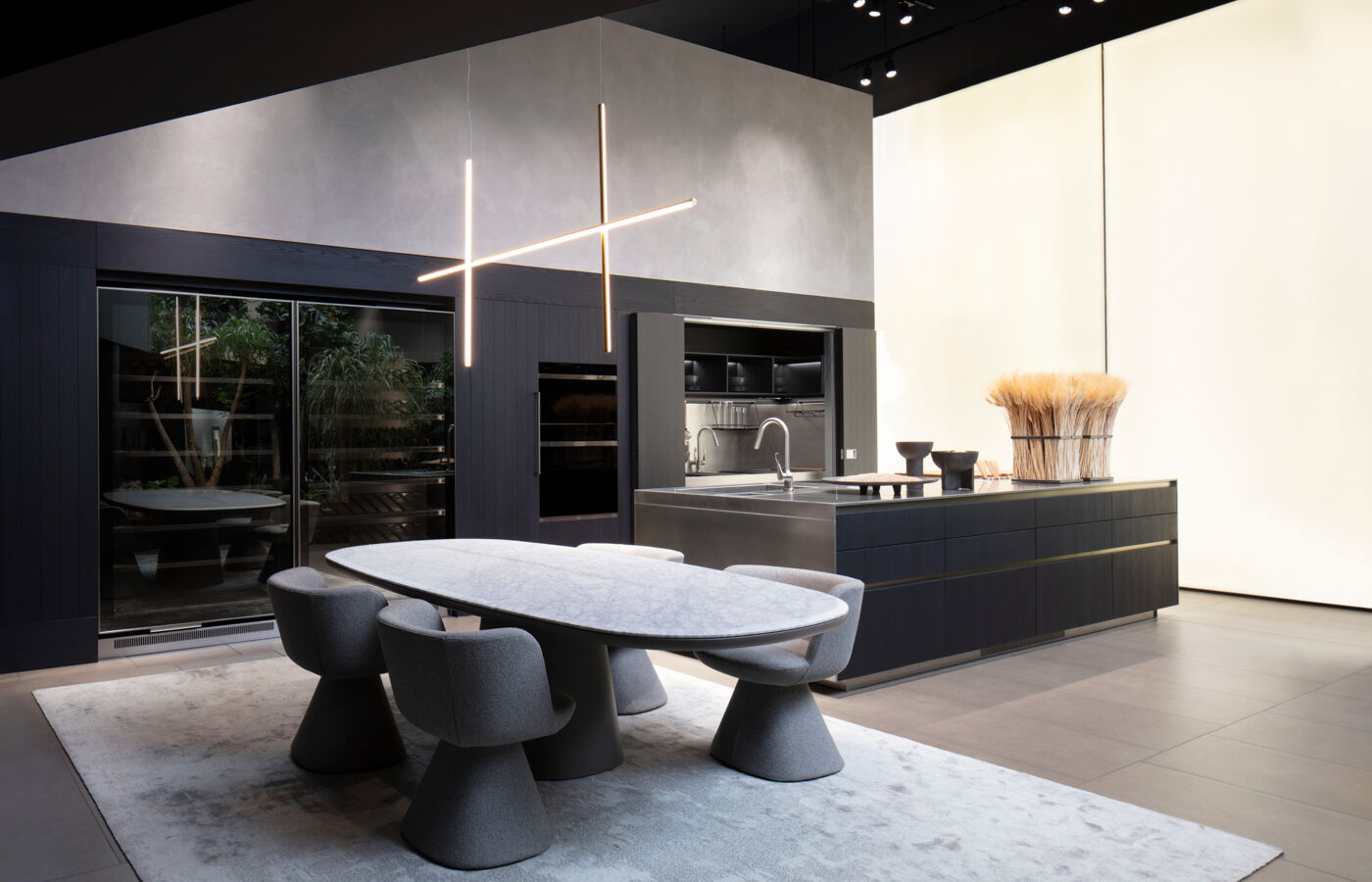 An Arclinea kitchen island in dark wood paired with a marble-topped dining table and sculptural grey chairs beneath crossed linear pendant lights
