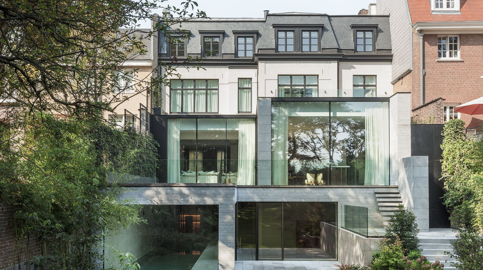 Rear facade of the Brussels townhouse combining a classic stone and slate-roofed elevation with a glazed contemporary extension overlooking a garden pool