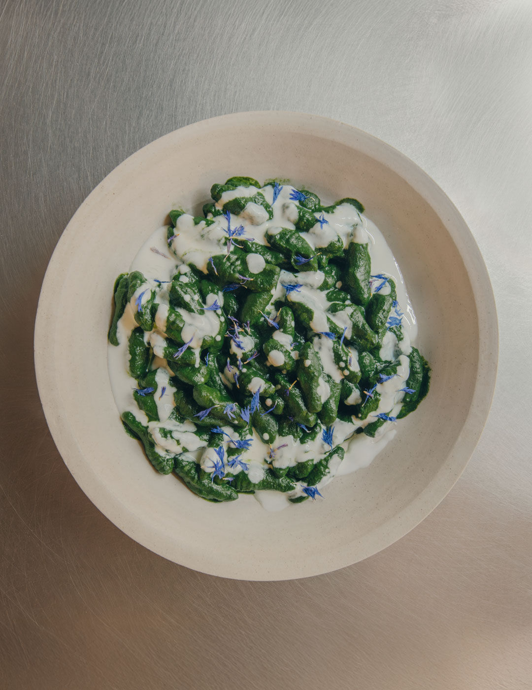 plated green pasta with creamy sauce and edible flowers, presented on a neutral ceramic plate