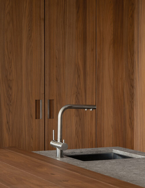 Arclinea kitchen Convivium detail of stainless faucet and stone worktop against wood panels