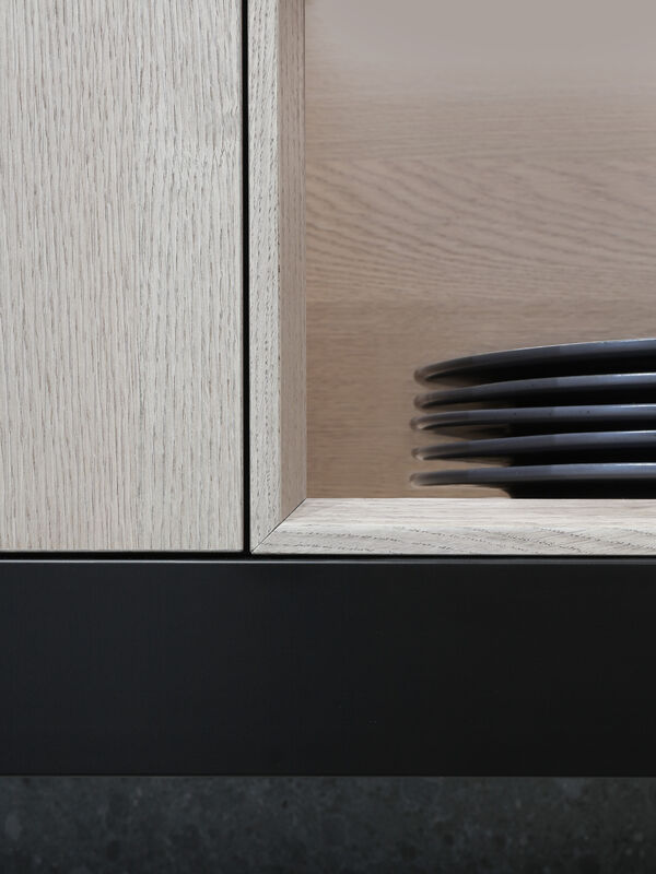 Close-up detail of the corner joint between a light wood cabinet and a marble shelf holding a stack of dark ceramic plates