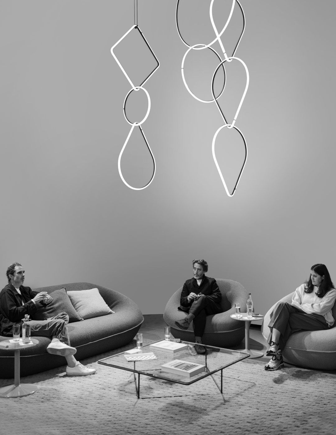 Three guests converse on sofas and an armchair beneath sculptural looping pendant lights during the Brompton Road opening event