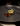 A single glazed piece of meat topped with delicate yellow flowers is plated minimally on a dark round plate