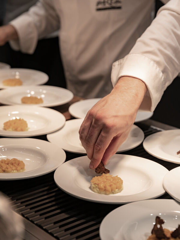 Chef placing crispy garnish on plates of mashed potato with truffle at MDW22 event