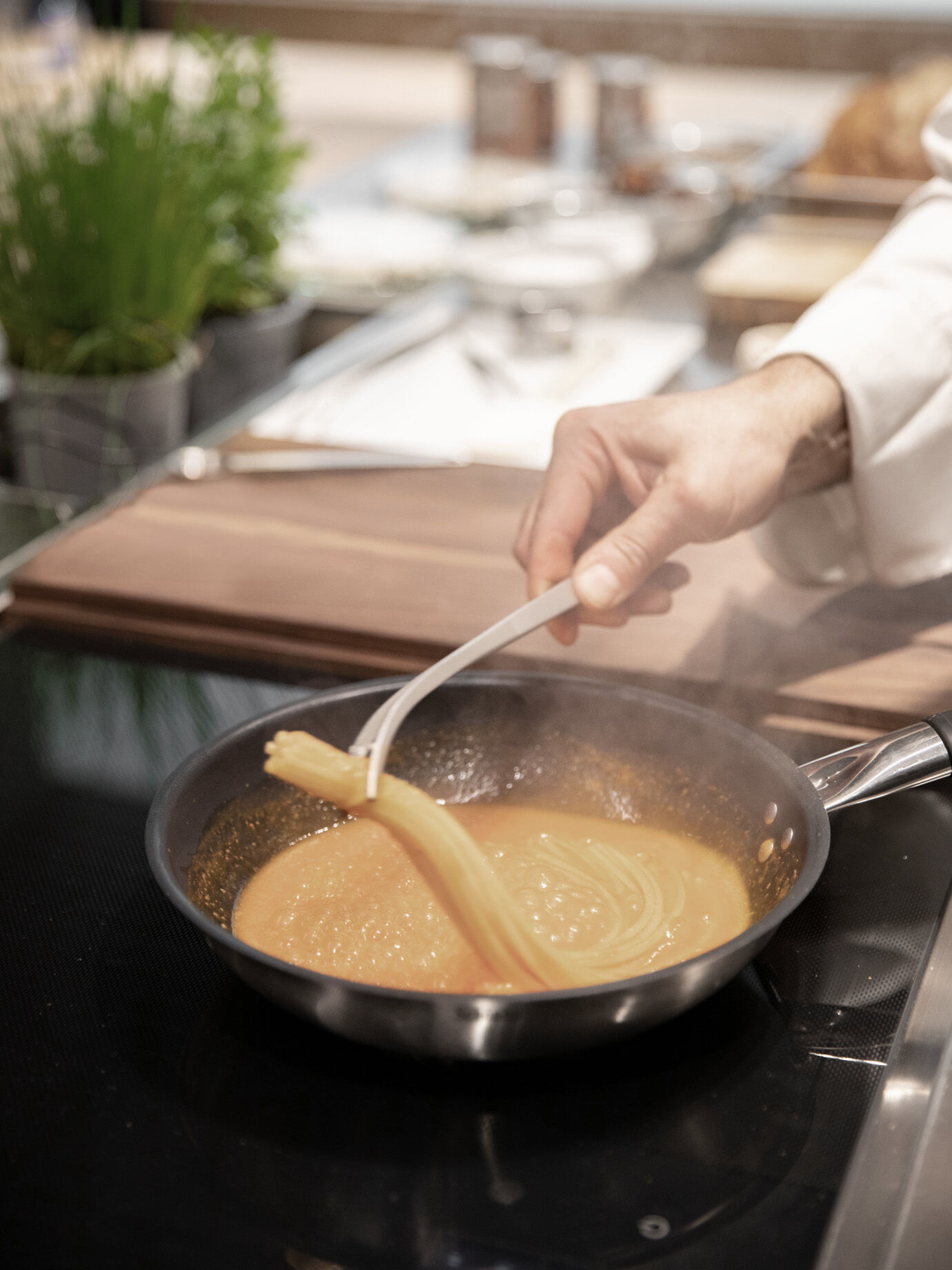Chef stirring golden sauce with fresh pasta in a pan on Arclinea induction cooktop