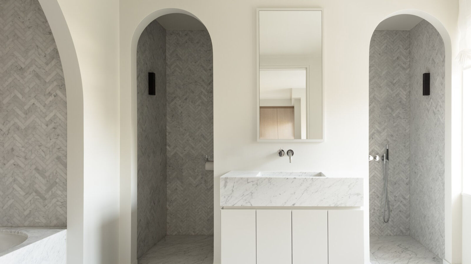 Showcase Townhouse DT Brussels | Marble bathroom with twin arched shower niches finished in herringbone tile, a freestanding marble vanity, and a mirrored cabinet between them