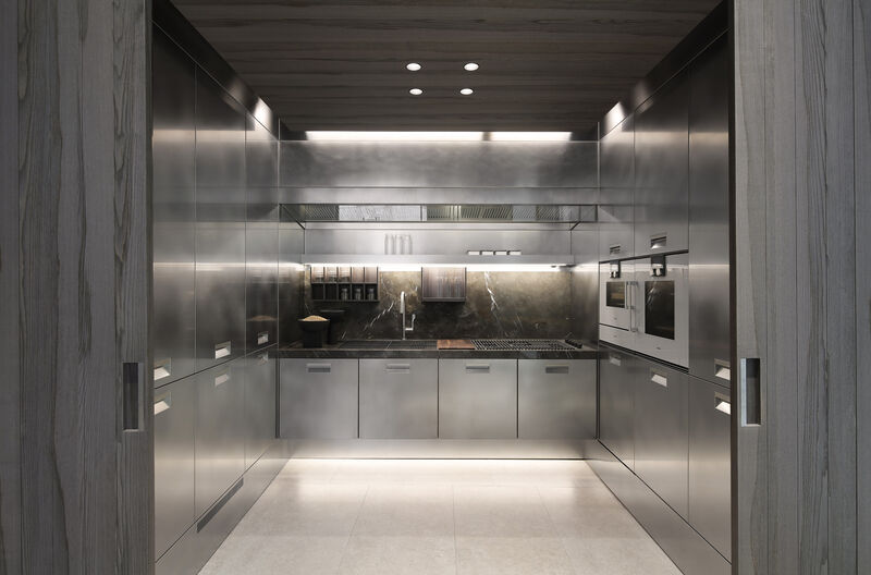 A stainless steel kitchen unit viewed through an open doorway, with black appliances, a marble backsplash and integrated cooktop and sink