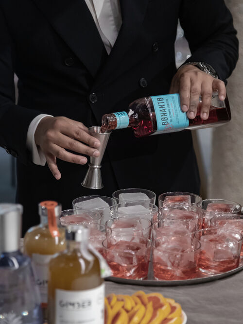 Bartender measuring red aperitivo liqueur into jigger over glasses with ice