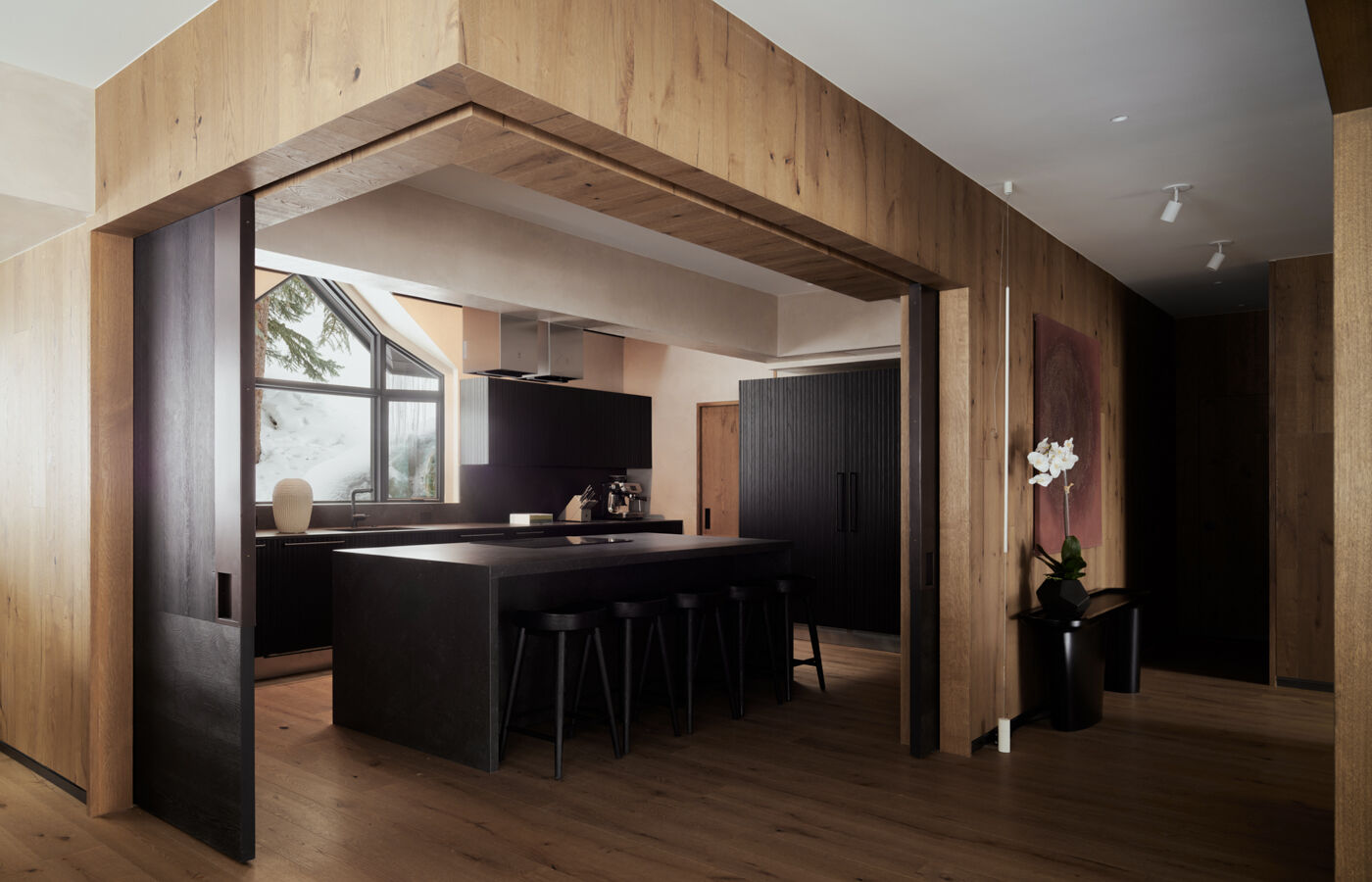 Arclinea kitchen with black marble island, bar stools, black ash wood finishes, and natural light from a snowy window