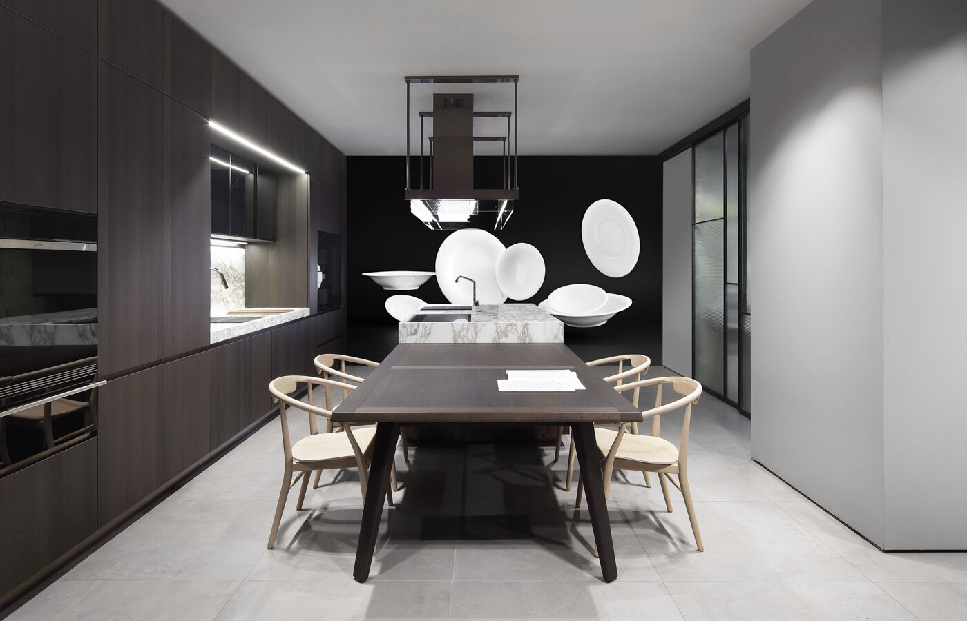 Dark wood kitchen with a wooden dining table, woven chairs and an artistic display of white ceramic plates suspended on a black wall