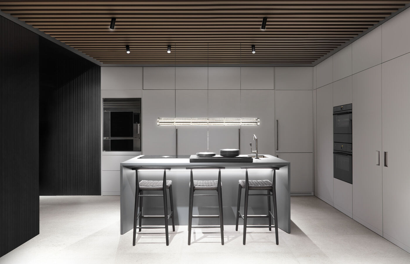 Straight on view of the grey kitchen island and bar seating area, with backlit glass display shelving and full height cabinetry along the rear wall