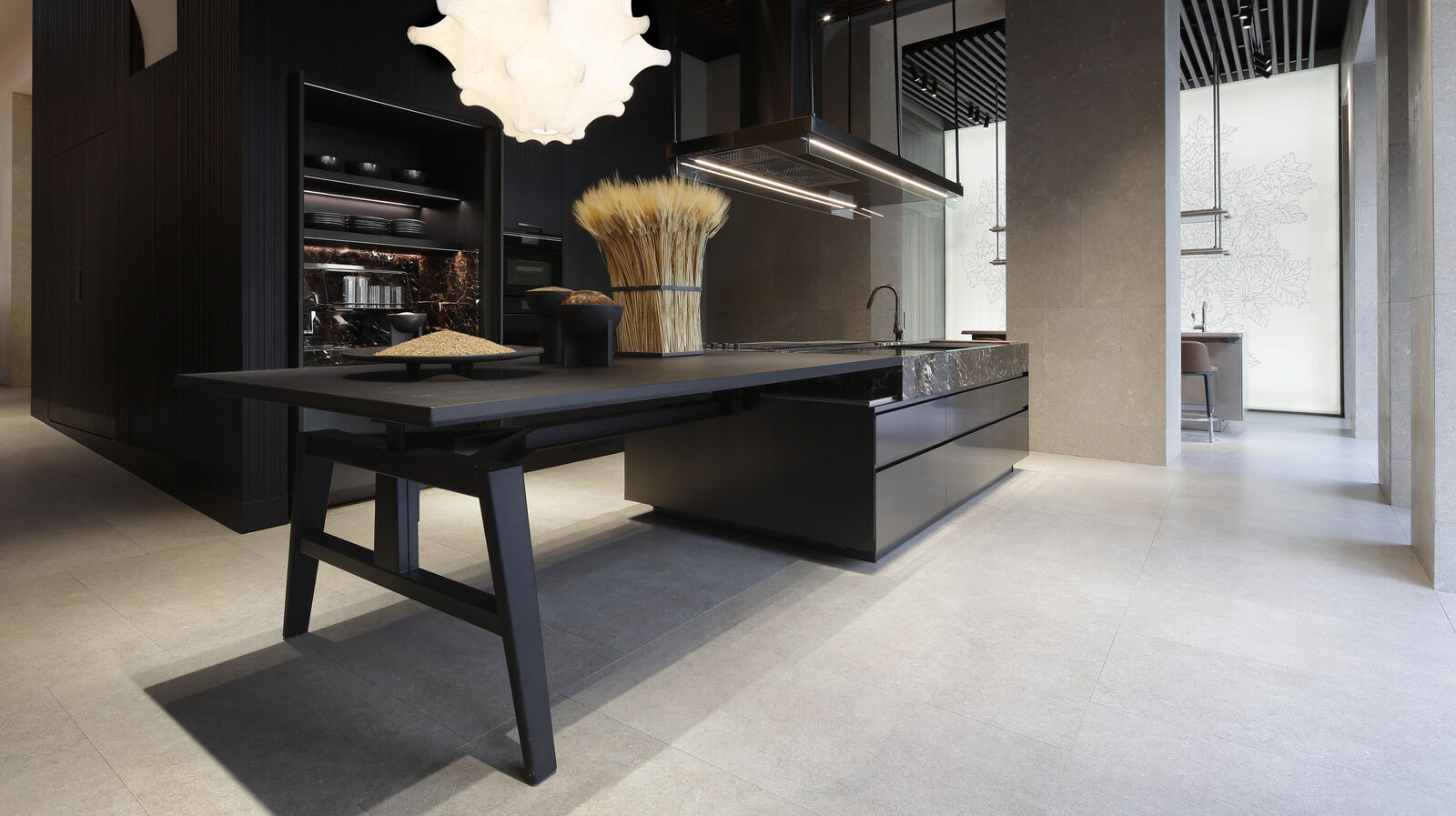 A black dining table with modern chairs positioned next to a dark marble topped kitchen island, with wheat sheaves and pendant lighting overhead