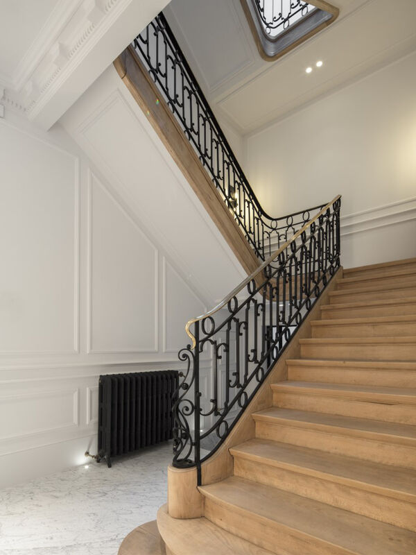 Ornate wooden staircase with black wrought-iron railing and a skylight above, leading down to a marble-floored entrance hall with a period radiator