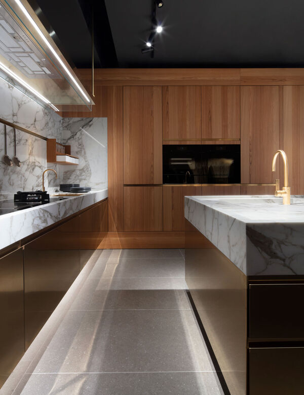 A wood-panelled Arclinea kitchen with a marble island and countertop, brass tap and integrated appliances along the back wall