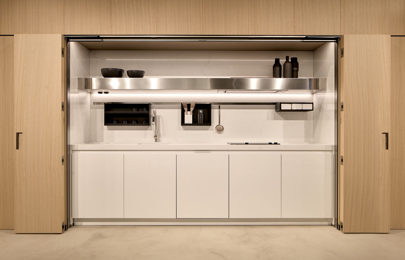 Arclinea Thea kitchen hidden workspace with open doors, white cabinetry and stainless hood