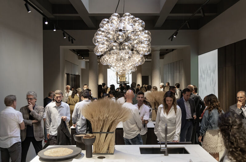 Guests gathered around wheat sheaf decorated kitchen island under sphere chandelier at MDW22 event