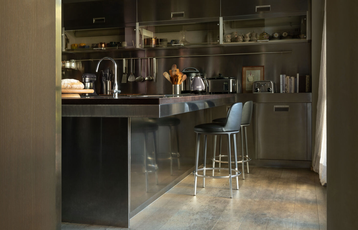 Steel Arclinea kitchen island with bar stools, bread board and countertop appliances seen from the doorway