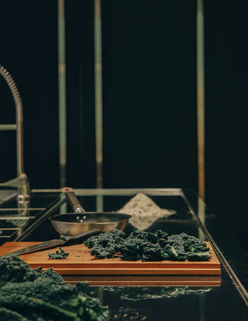 fresh kale chopped on a wooden board beside a pan, set on a Arclinea kitchen worktop