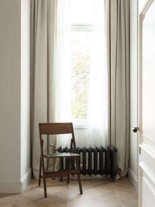 Wooden folding chair beside curtained window and vintage radiator