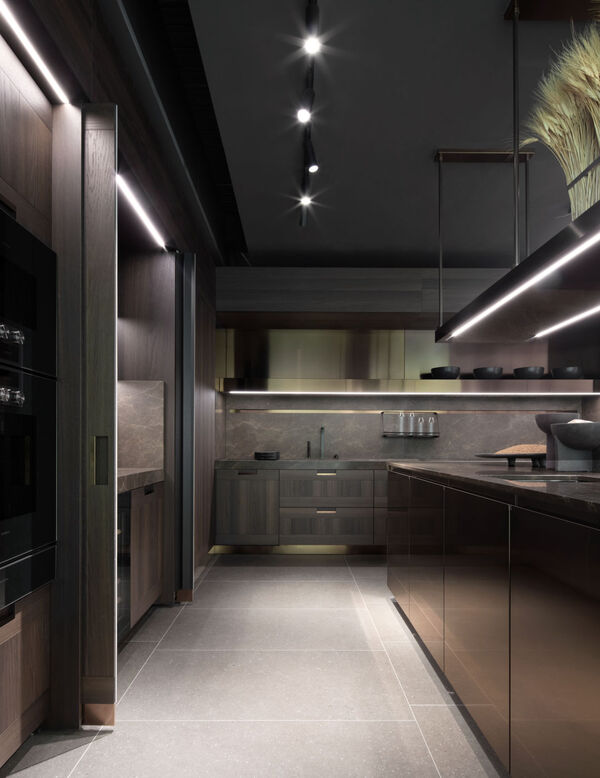 A dimly lit corridor-style Arclinea kitchen with dark wood cabinetry, integrated lighting strips and a stone worktop in the Brompton Road showroom
