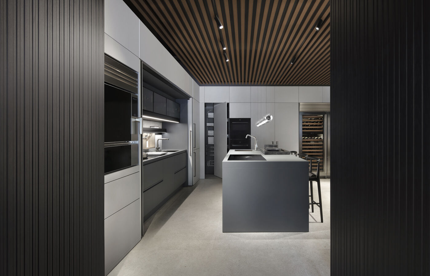 Grey kitchen composition with an open pantry cabinet revealing internal storage, flanked by tall cabinetry and a central island with bar seating beyond