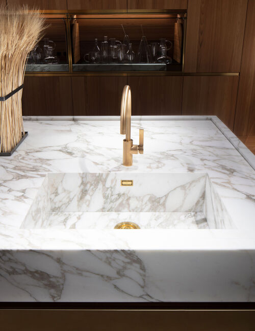 Close-up of a marble kitchen sink with a brass gooseneck tap and matching brass drain fittings