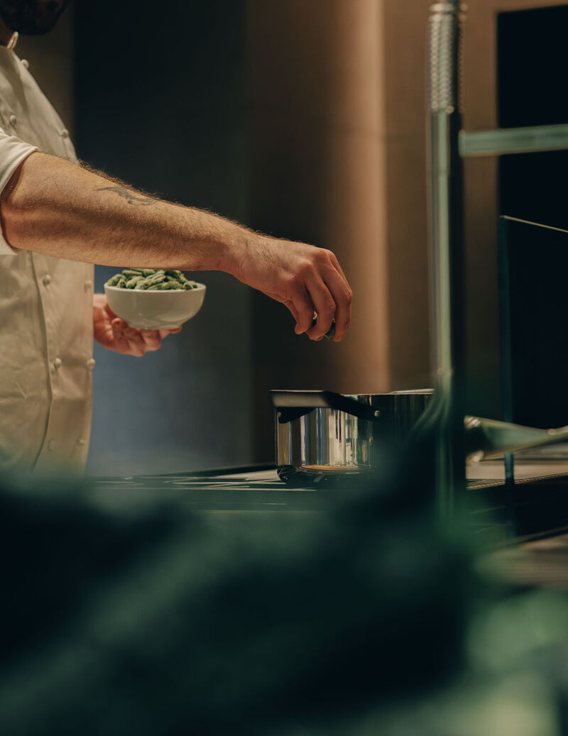 chef fabrizio bonelli of fieno seasoning a pot with fresh ingredients during cooking in a contemporary Arclinea kitchen