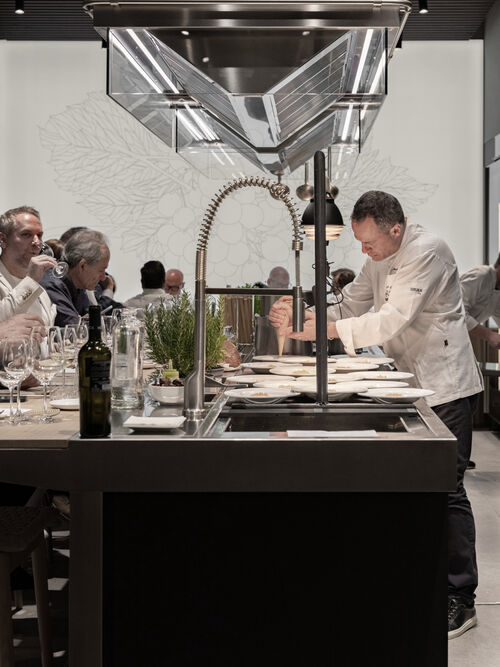 Chef pouring sauce over plated dishes at Arclinea kitchen sink station in front of seated guests