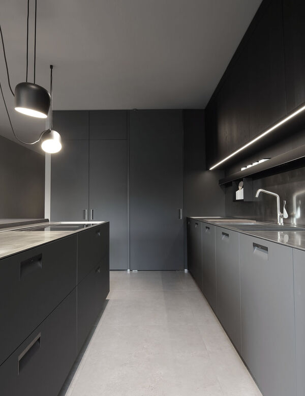Narrow galley style showroom kitchen in dark tones with pendant lights, stone flooring and two facing counters