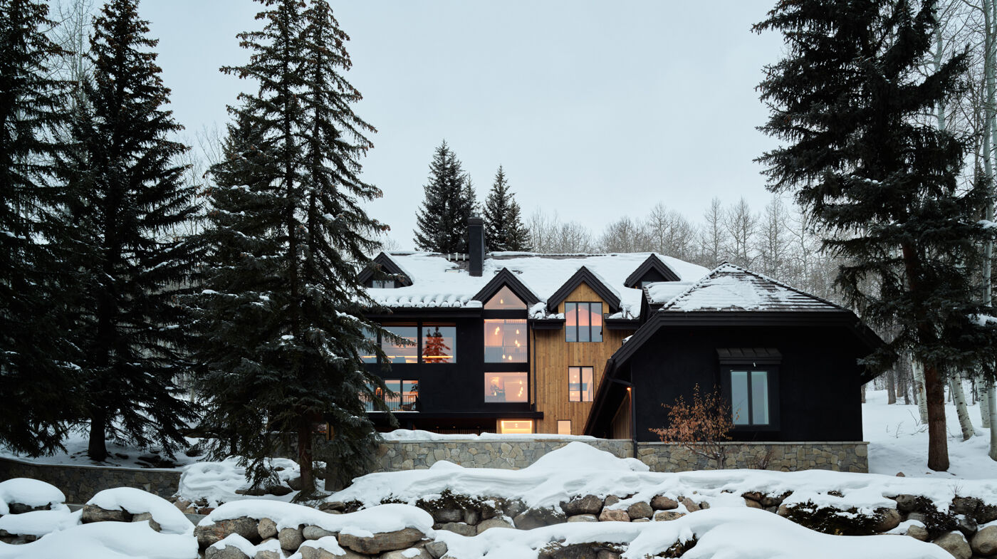 Modern mountain home with dark wood facade, large windows, and snow-covered pine trees Arclinea residential project